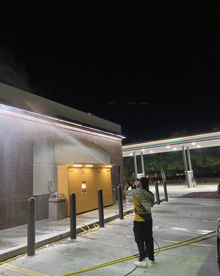 Man pressure washing the outside of a 7/11 gas station building that had algae build up on the exterior walls.