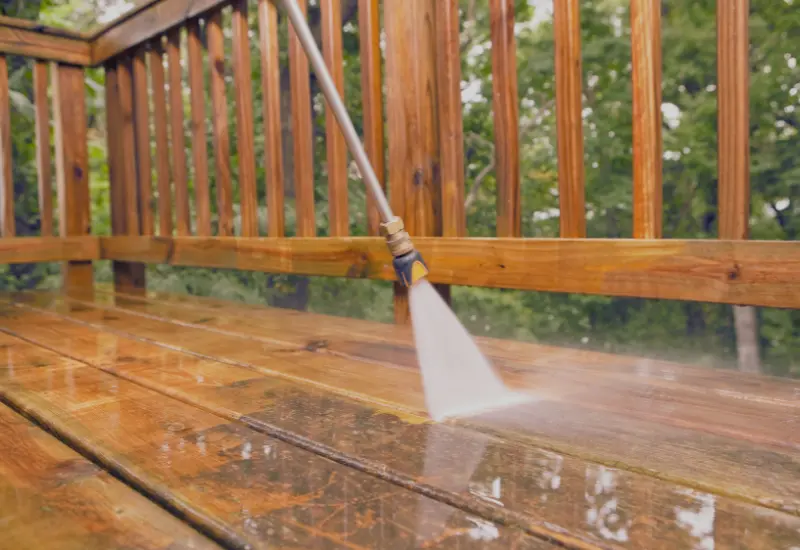 Person pressure washing a wood deck